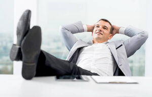 Smiling businessman resting his legs on the desk and enjoying himself.